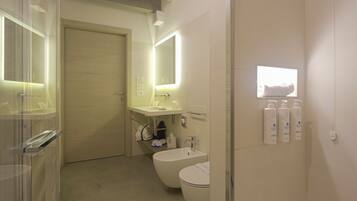 Uma casa de banho moderna com sanita, bidé e lavatório, equipada com espelho e iluminada por luzes de parede.