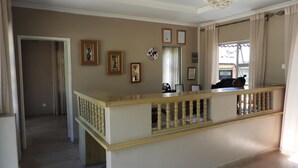 A spacious living area with a wooden railing, a chandelier, and framed pictures on the wall.