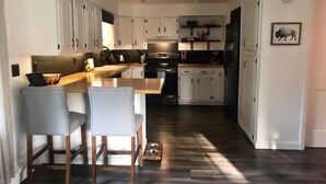 Een moderne keuken met witte kastjes, een houten kookeiland met barstoelen, een ingebouwde oven en een koelkast.