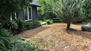 Een huis met een donkere gevel, een kleine voortuin met een boom, en een pad dat naar het huis leidt.