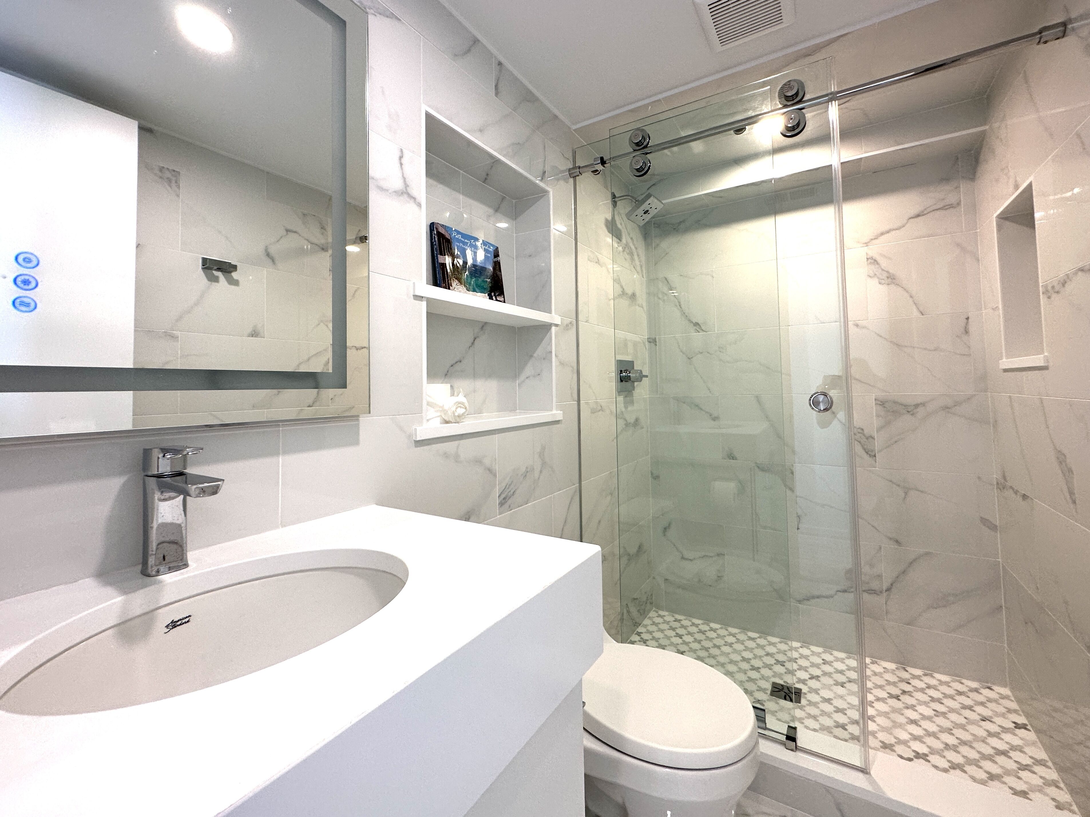 Casa de banho moderna com lavatório branco, sanita e cabine de duche em vidro.