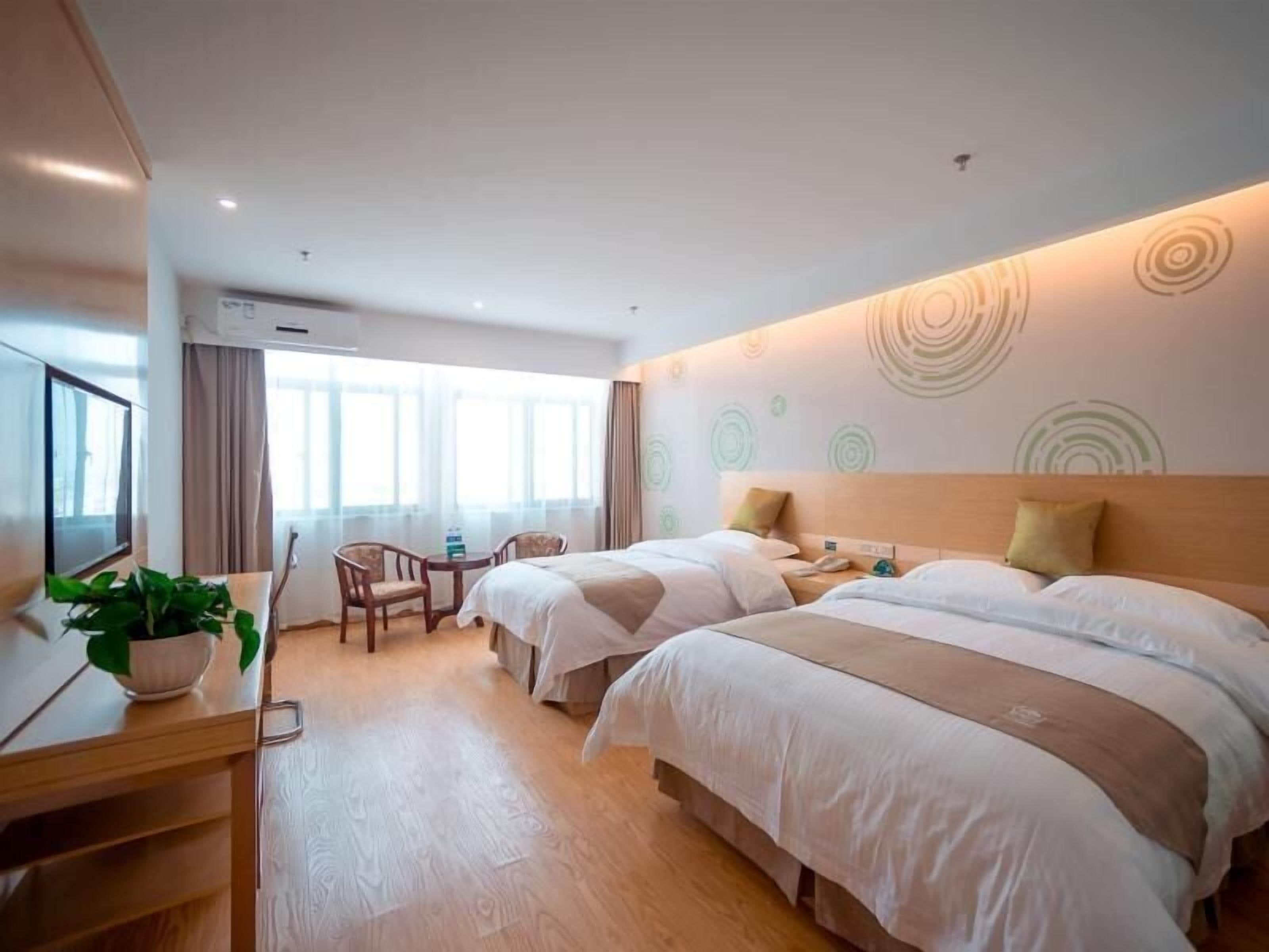 Habitación de hotel con dos camas, un escritorio, una silla, un televisor y un ventanal grande.