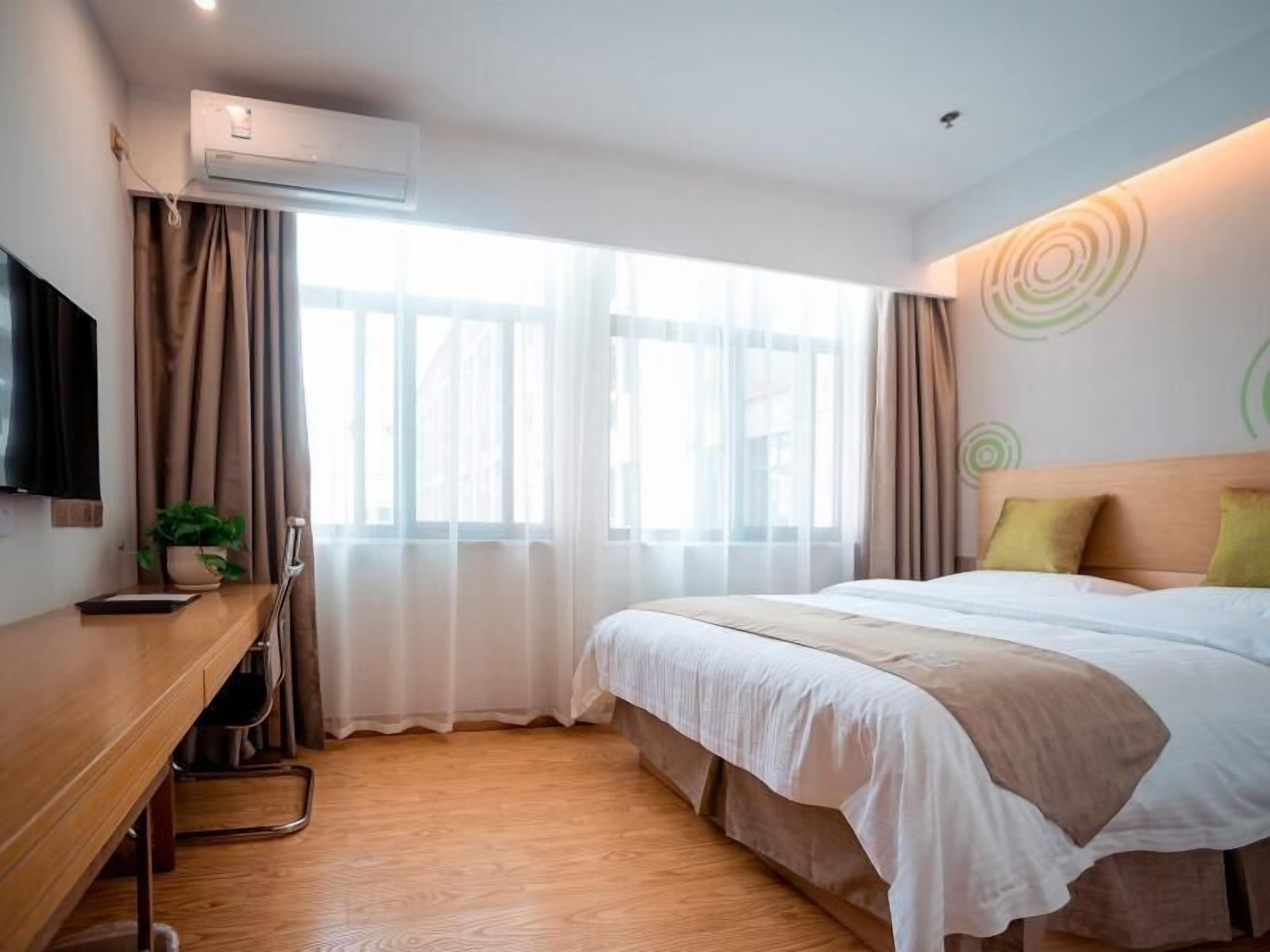 Een hotelkamer met een bed, bureau, stoel, airconditioning en een televisie.
