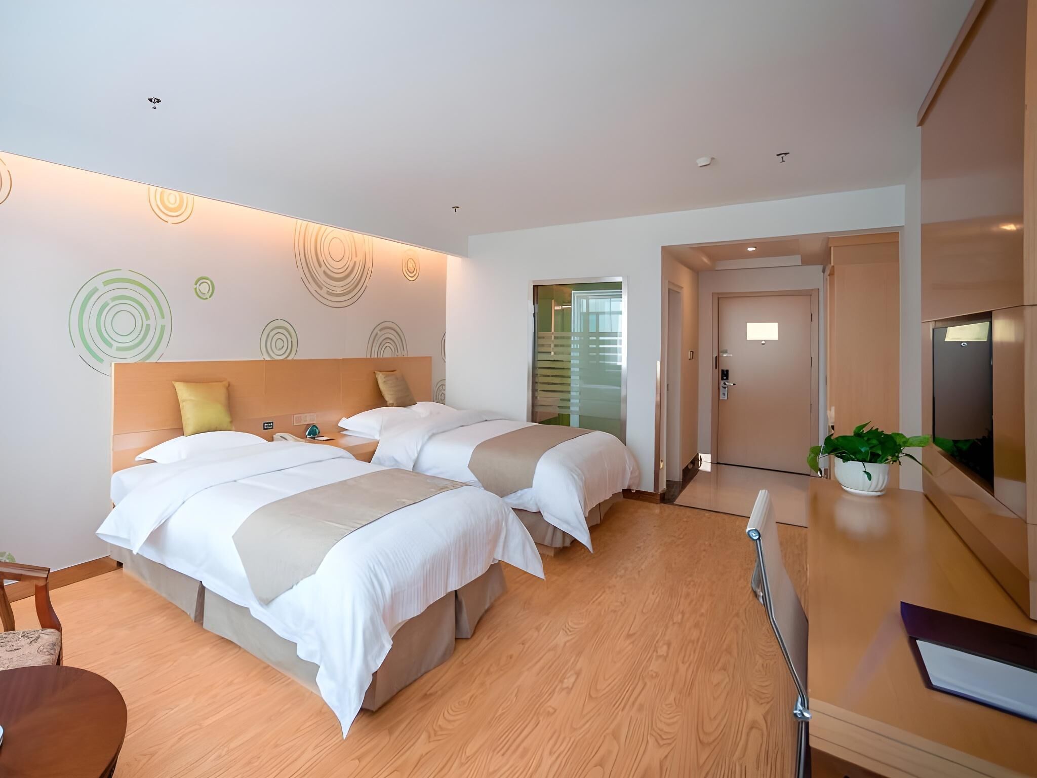 Habitación de hotel con dos camas, un escritorio, una silla, una planta y una puerta que da a un balcón.