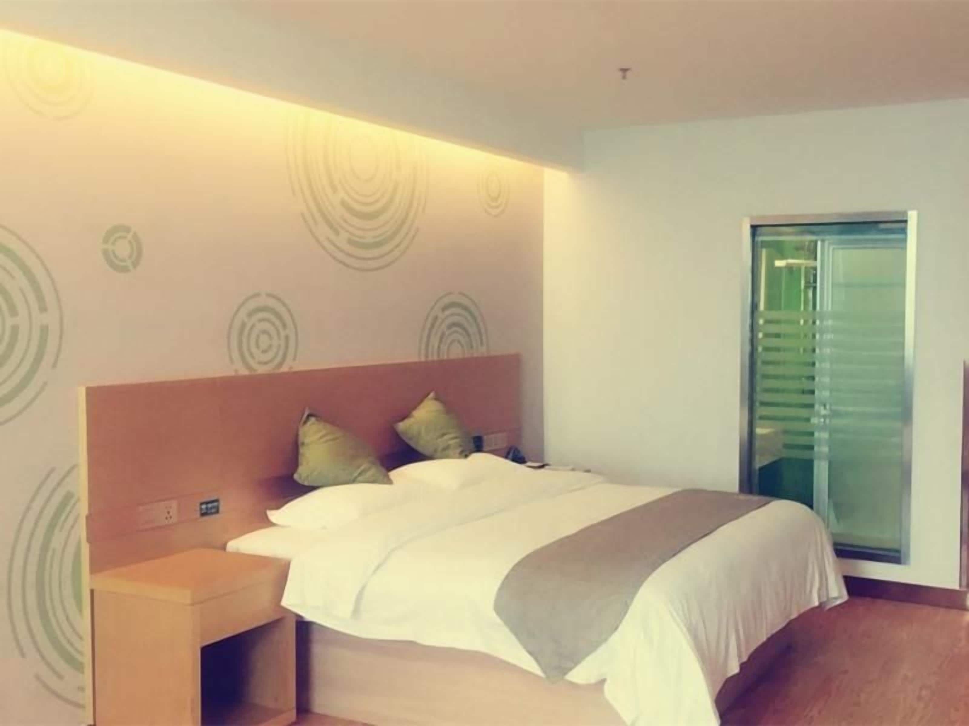 Ein modernes Hotelzimmer mit einem Bett, einem Nachttisch und einem Fenster mit Jalousien.