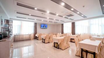 Un salón de conferencias de hotel con varias mesas y sillas, un televisor de pantalla plana y un ventanal grande.