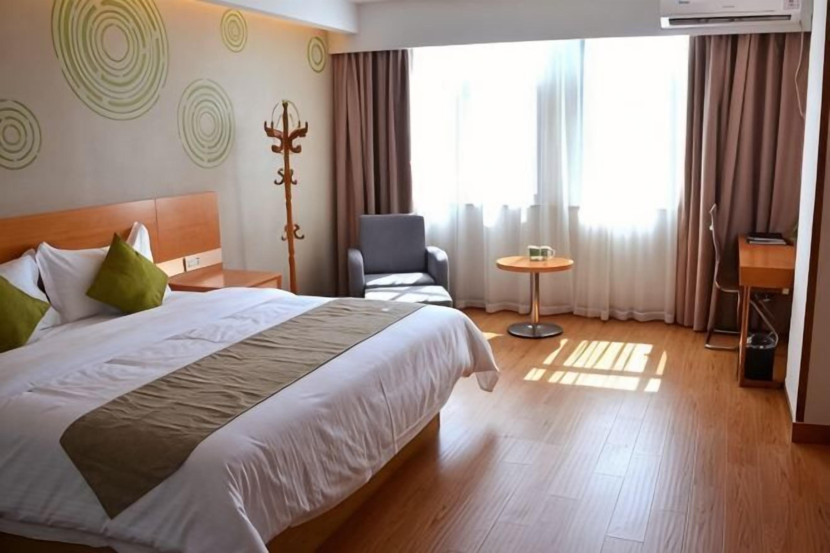 Una habitación de hotel con una cama, una silla, una mesita y un ventanal con cortinas.