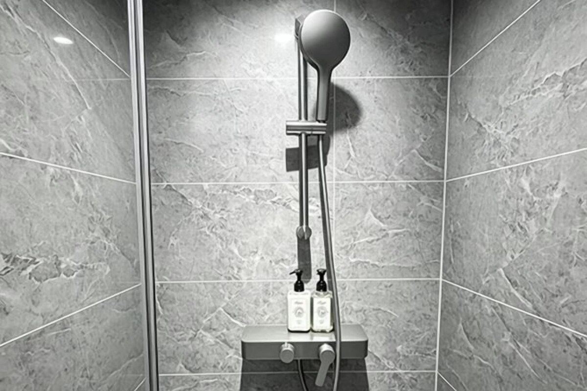 A modern shower with a handheld showerhead, a control panel, and a wall-mounted faucet.