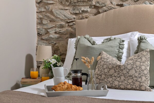 A neatly made bed with pillows, a tray with croissants and coffee, a cup of coffee, and a glass of orange juice.
