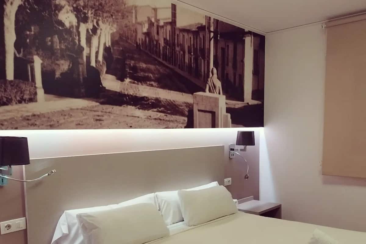A neatly made bed with white linens, a bedside table with a lamp, and a wall-mounted TV.