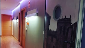 A hotel corridor with wooden flooring, a wall-mounted fire alarm, and a door with a number sign. - Hello Villarreal Suites (Villarreal)