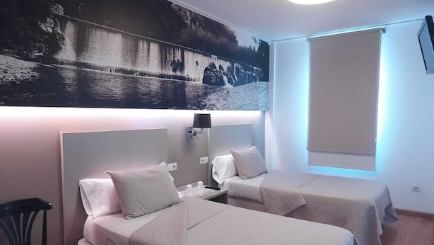 A hotel room with two beds, a chair, a wall-mounted TV, and a large window. - Hello Villarreal Suites (Villarreal)