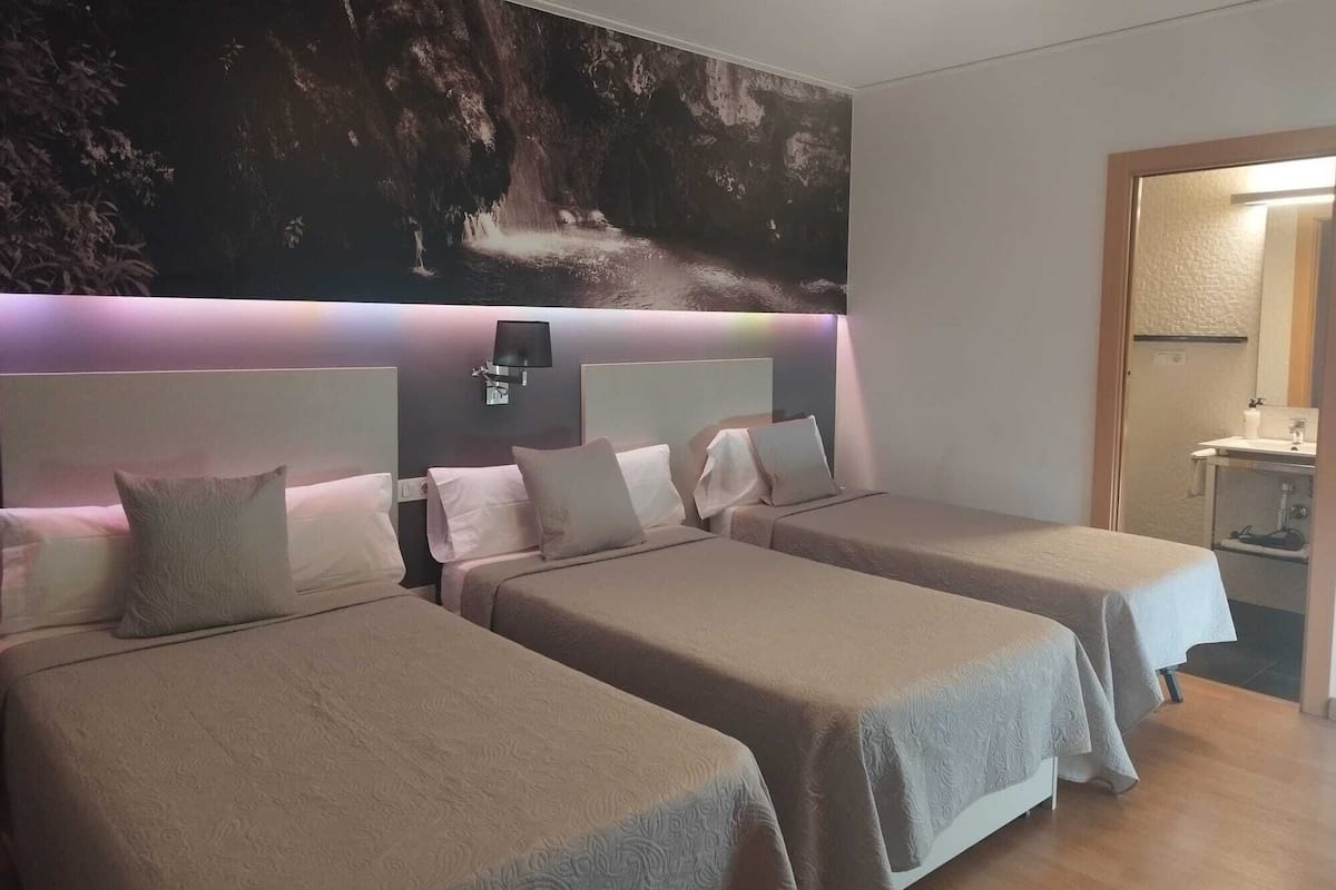 A hotel room with two beds, a large wall mural, a bedside lamp, and a bathroom visible through an open door.