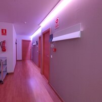 Un pasillo con suelo de madera, puertas rojas y un extintor en la pared.
