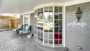 A covered patio with a curved glass enclosure, outdoor seating, and a 'welcome' sign on the wall. - Stay Near All Family Entertainment in Dallas (Richardson)