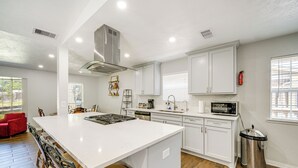 A modern kitchen with white cabinetry, a large island, and a dining area with chairs. - Stay Near All Family Entertainment in Dallas (Richardson)