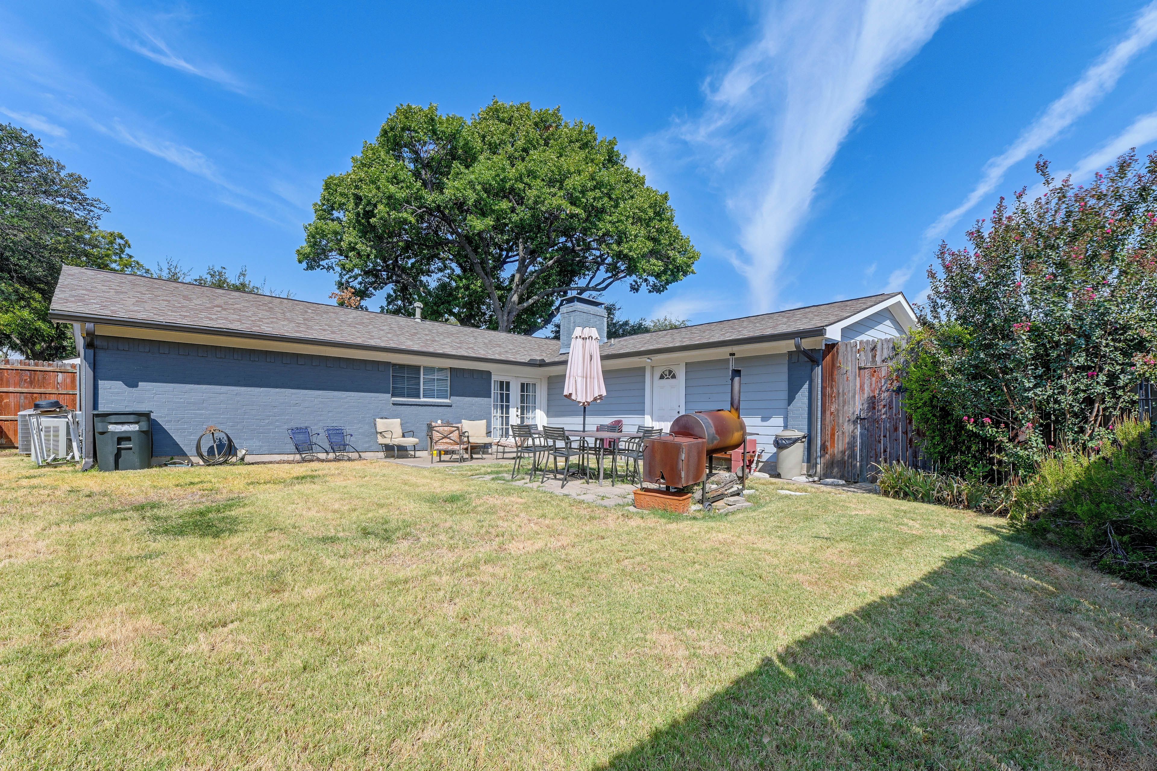 A residential backyard with a barbecue grill, outdoor furniture, and a large tree.