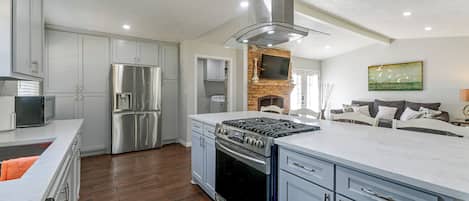 A modern kitchen with stainless steel appliances, a brick fireplace, and a large island.