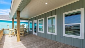 A covered deck with wooden flooring, a railing, and a seating area with chairs.