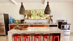 A modern kitchen with a large island, red bar stools, a stainless steel refrigerator, a built-in oven, and hanging pendant lights. - Casa Arenas, steps away from the ocean! (Provincia de Puntarenas)