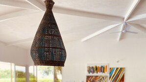 A modern living room with a dining area, featuring a large woven pendant light, a blue vase with a plant, and a dining table with wooden trays. - Casa Arenas, steps away from the ocean! (Provincia de Puntarenas)