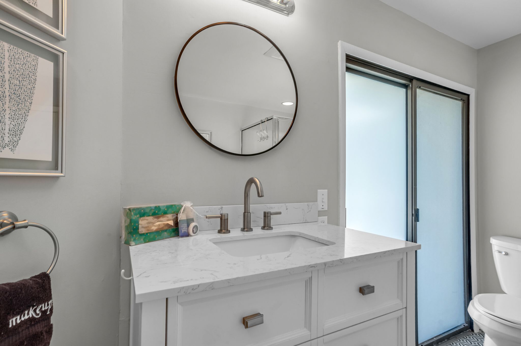 Une salle de bain moderne avec un meuble-lavabo blanc, un miroir rond et des toilettes.