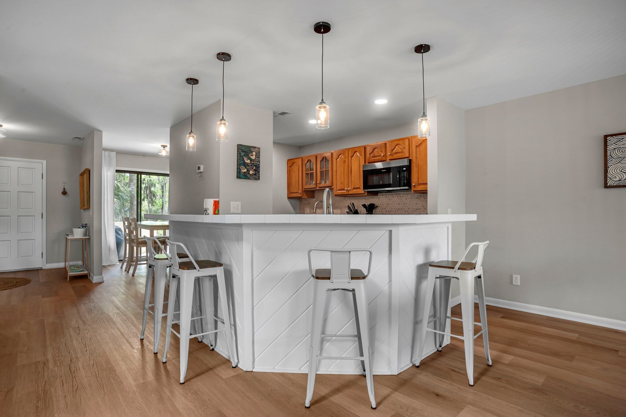 A modern kitchen with wooden cabinets, a central island with bar stools, pendant lighting, and a view of the dining area.