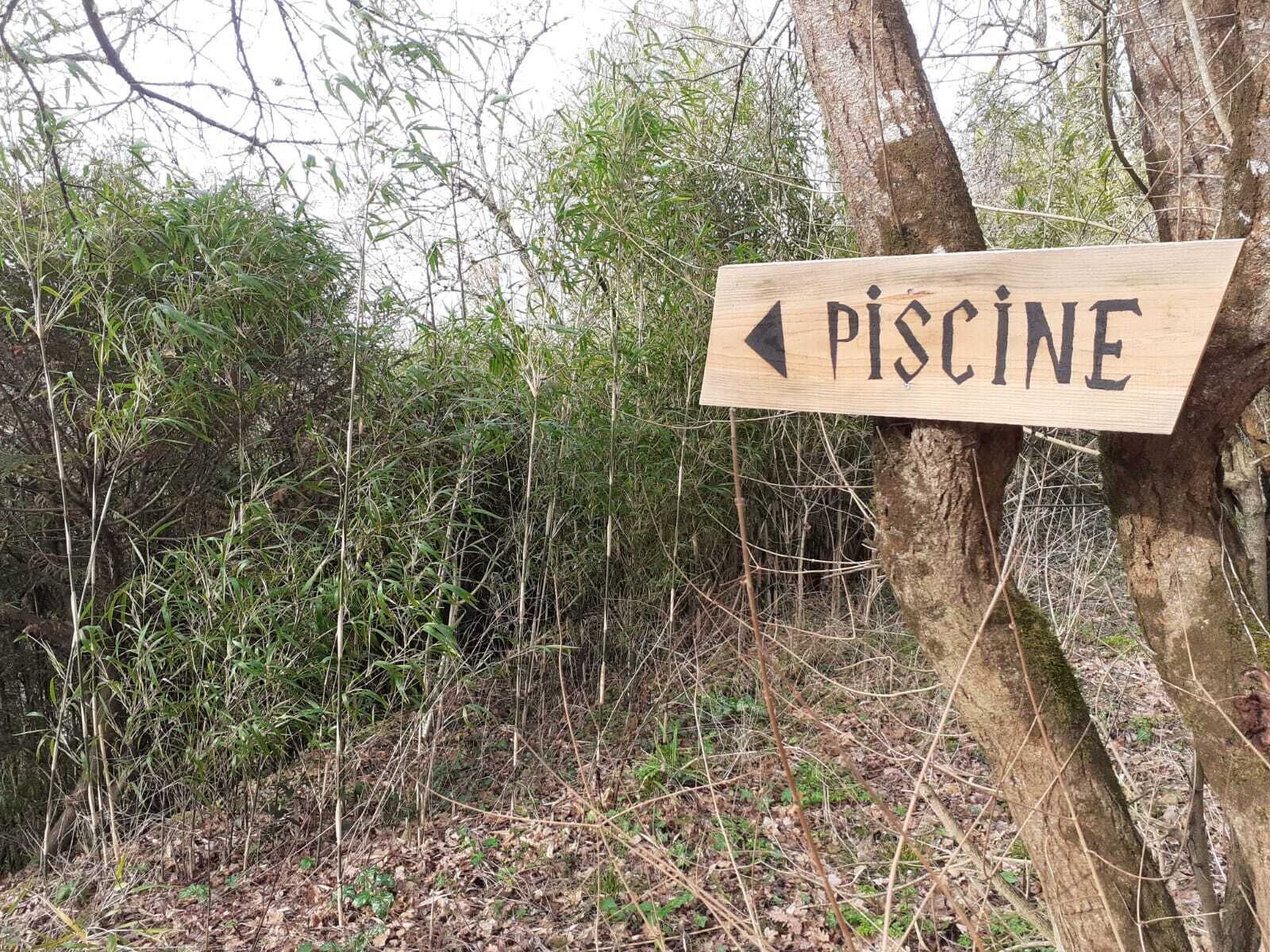 A wooden sign with an arrow pointing left, labeled 'PISCINE'.