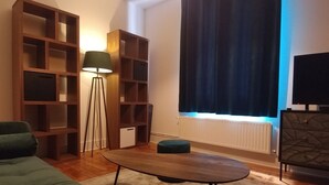 Una sala de estar con sofá, mesa de centro, lámpara de pie, televisor y estanterías empotradas.
