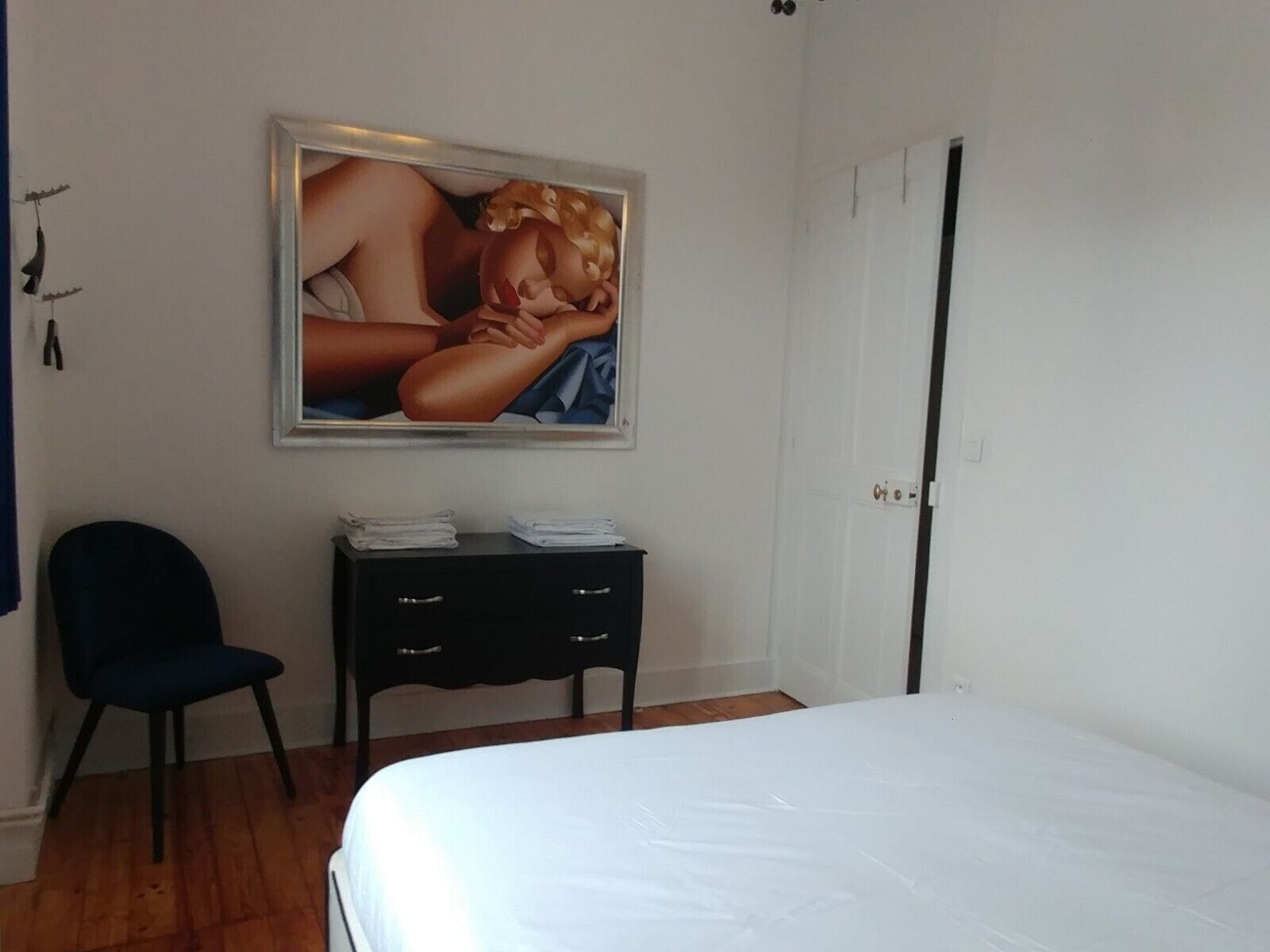 A bedroom with a bed, a desk with a chair, and a painting on the wall.