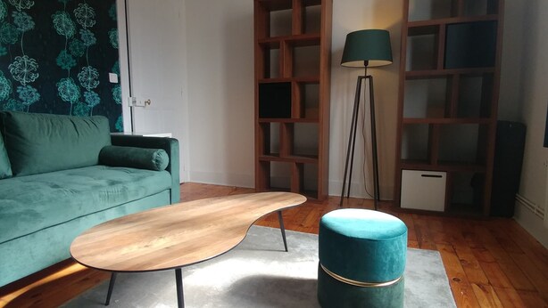 Una sala de estar con un sofá color turquesa, una mesa de centro de madera, un taburete turquesa y una lámpara de pie.
