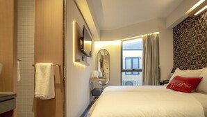 Een hotelkamer met een groot bed, een spiegel, een nachtkastje en een raam met gordijnen.