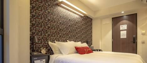 Une chambre d’hôtel avec un grand lit, une table de chevet, une horloge et un mur recouvert d’un papier peint à motifs.