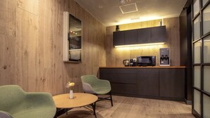 Een moderne keuken met houten kastjes, een koffieapparaat en een kleine eethoek met twee stoelen en een tafel.