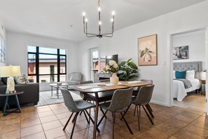 A modern living room with a dining area, large windows, and a chandelier.
