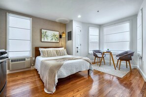 Une chambre à coucher comprenant un lit, un bureau, deux chaises, une fenêtre et une lampe fixée au mur.