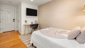 Une chambre à coucher comprenant un lit, un bureau, une chaise, un téléviseur fixé au mur et une porte avec un panneau indiquant la sortie de secours.