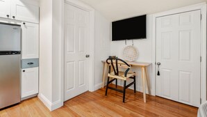 A kitchen with white cabinets, a built-in refrigerator, a wooden dining table with a chair, and a wall-mounted TV. - Dusk Suite at The Hygge House, Dusk Suite at The Hygge House (Newburyport)