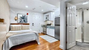 A compact bedroom with a bed, a bedside lamp, and a wall-mounted TV. Adjacent to the bedroom is a kitchenette with a microwave, stove, and refrigerator. - Dusk Suite at The Hygge House, Dusk Suite at The Hygge House (Newburyport)