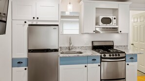 A compact kitchen with white cabinets, a stainless steel refrigerator, a microwave, a sink, and a stove.