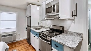 A compact kitchen with white cabinets, a stainless steel stove, a microwave, and a granite countertop.