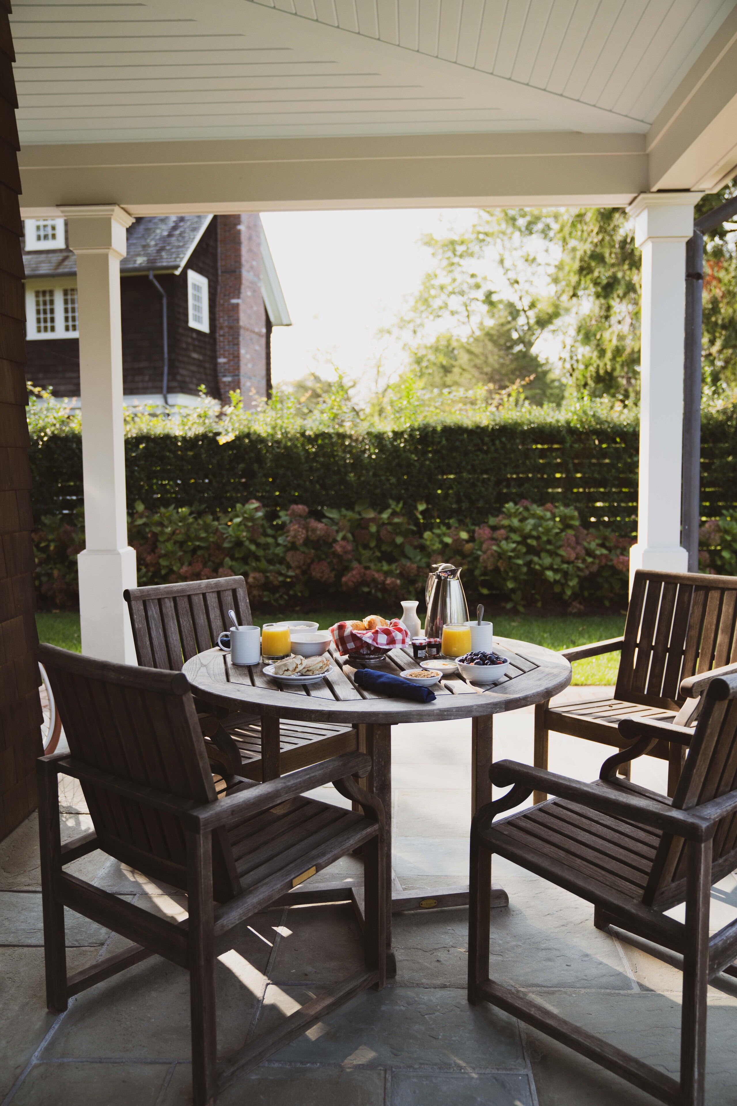 A covered patio with a round table set for breakfast, surrounded by wooden chairs.