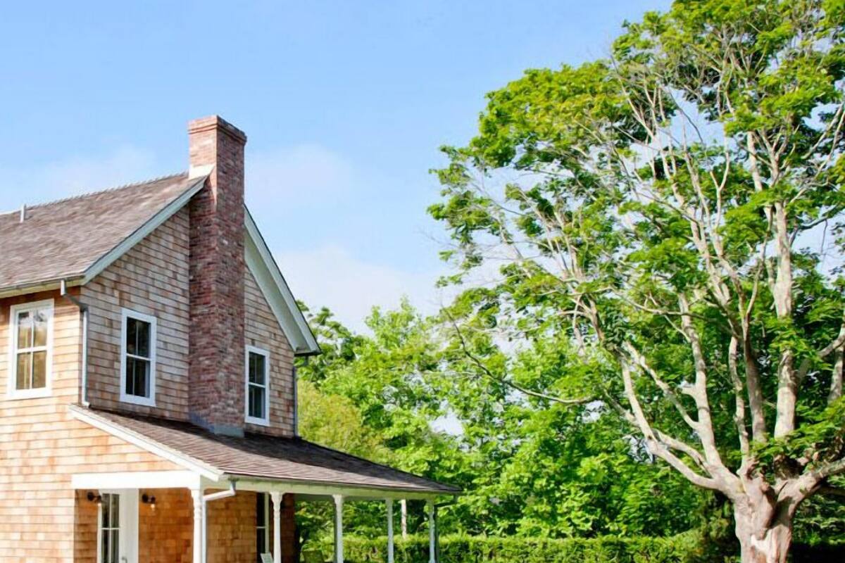 A two-story house with a brick exterior, a covered porch, and a large tree in the yard.