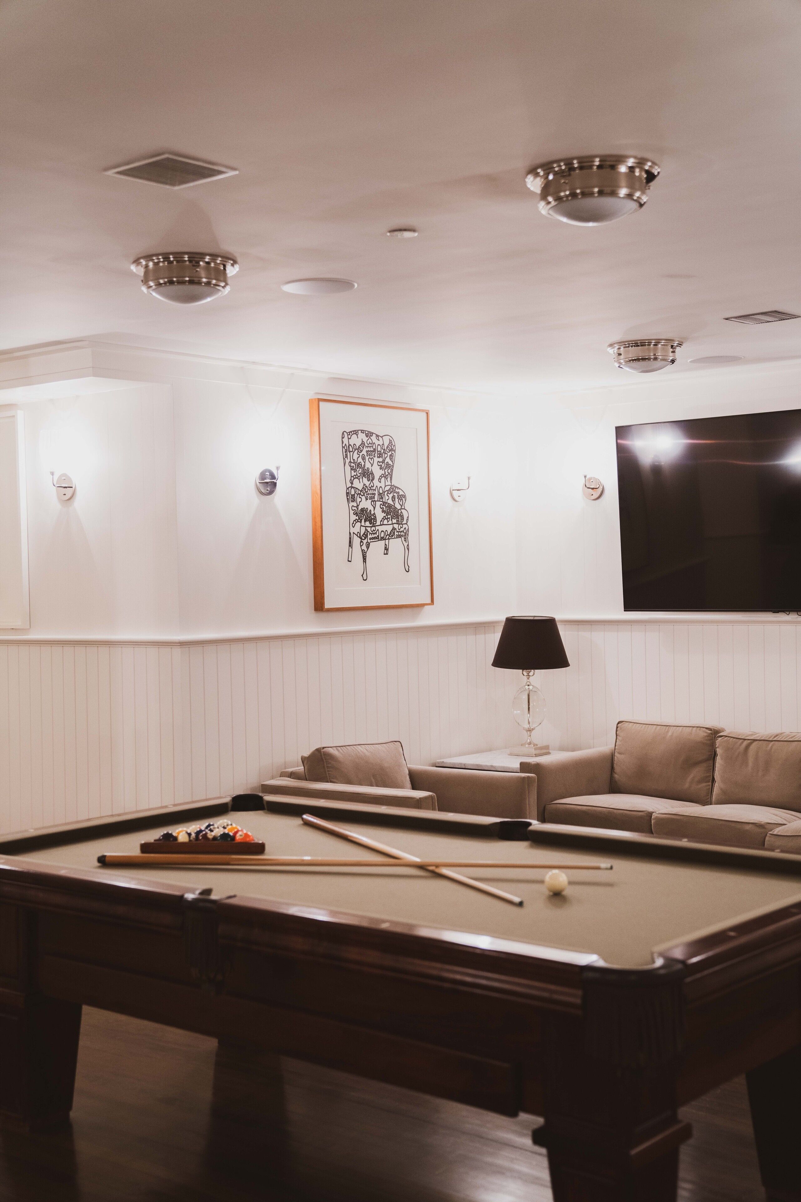 A pool table in a room with a sofa, a framed picture, and a television on the wall.