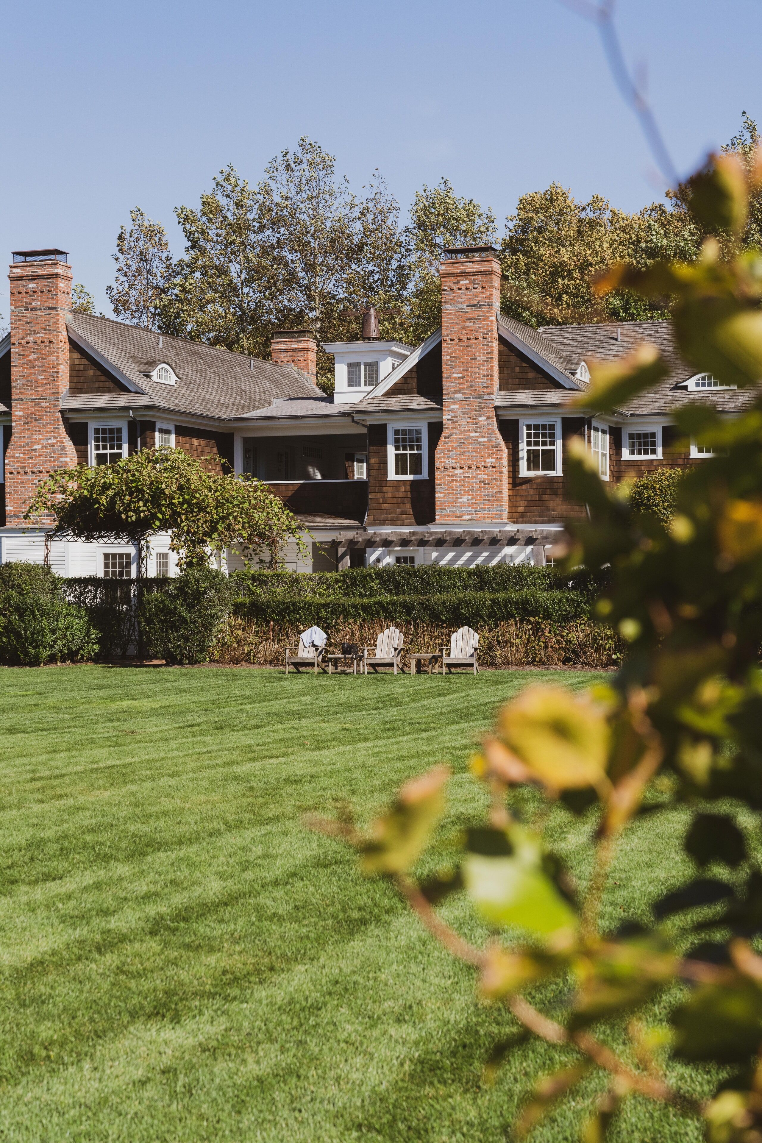A large brick house with a well-maintained lawn and two Adirondack chairs.