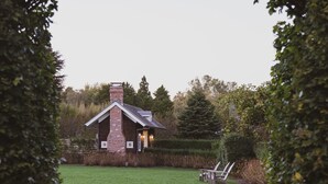 A small brick house with a chimney, surrounded by a well-maintained lawn and trees. - The Reform Club (Amagansett)