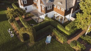 A two-story house with a covered patio and a small garden area. - The Reform Club (Amagansett)