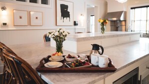 A modern kitchen with a marble countertop, a coffee maker, and a fruit tray. - The Reform Club (Amagansett)