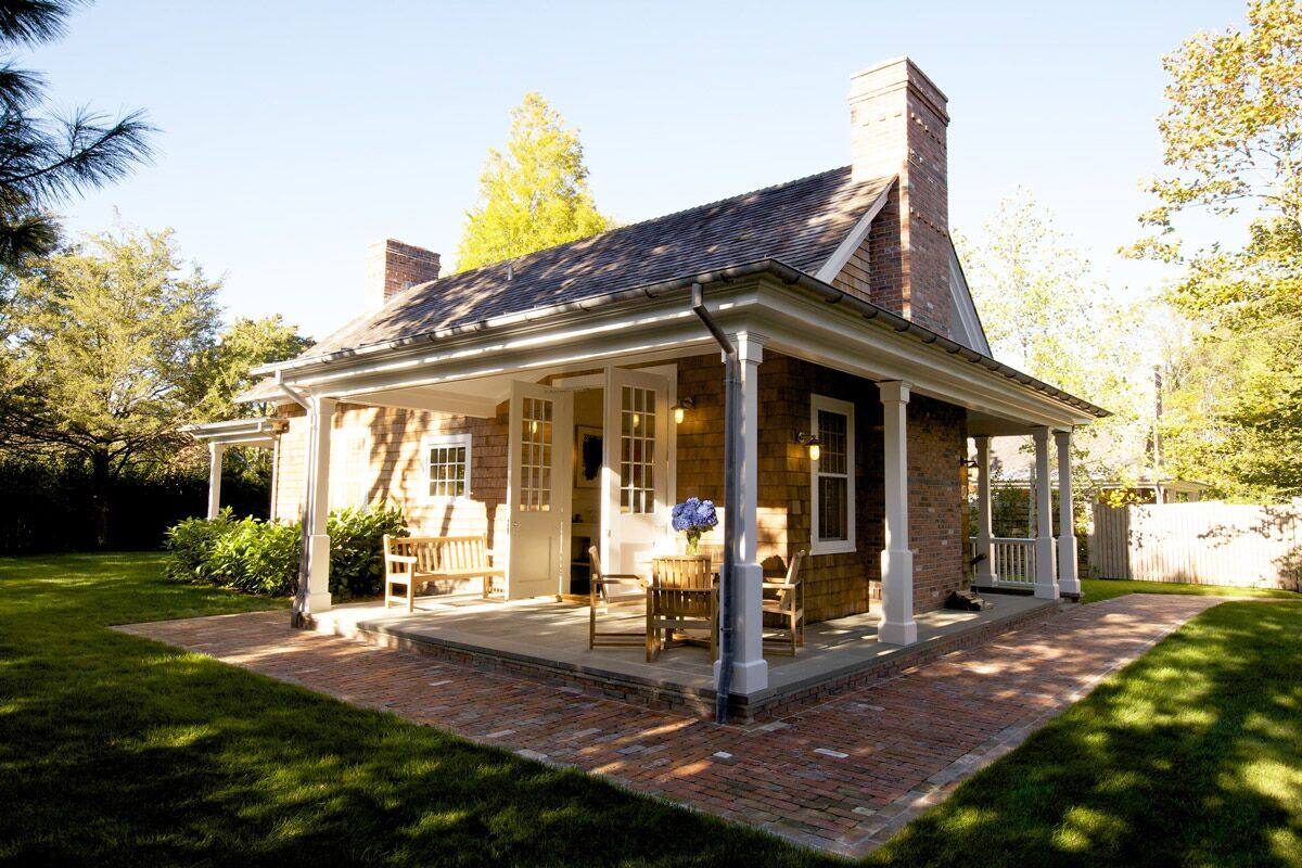 A brick house with a covered porch, a chimney, and a well-maintained lawn.