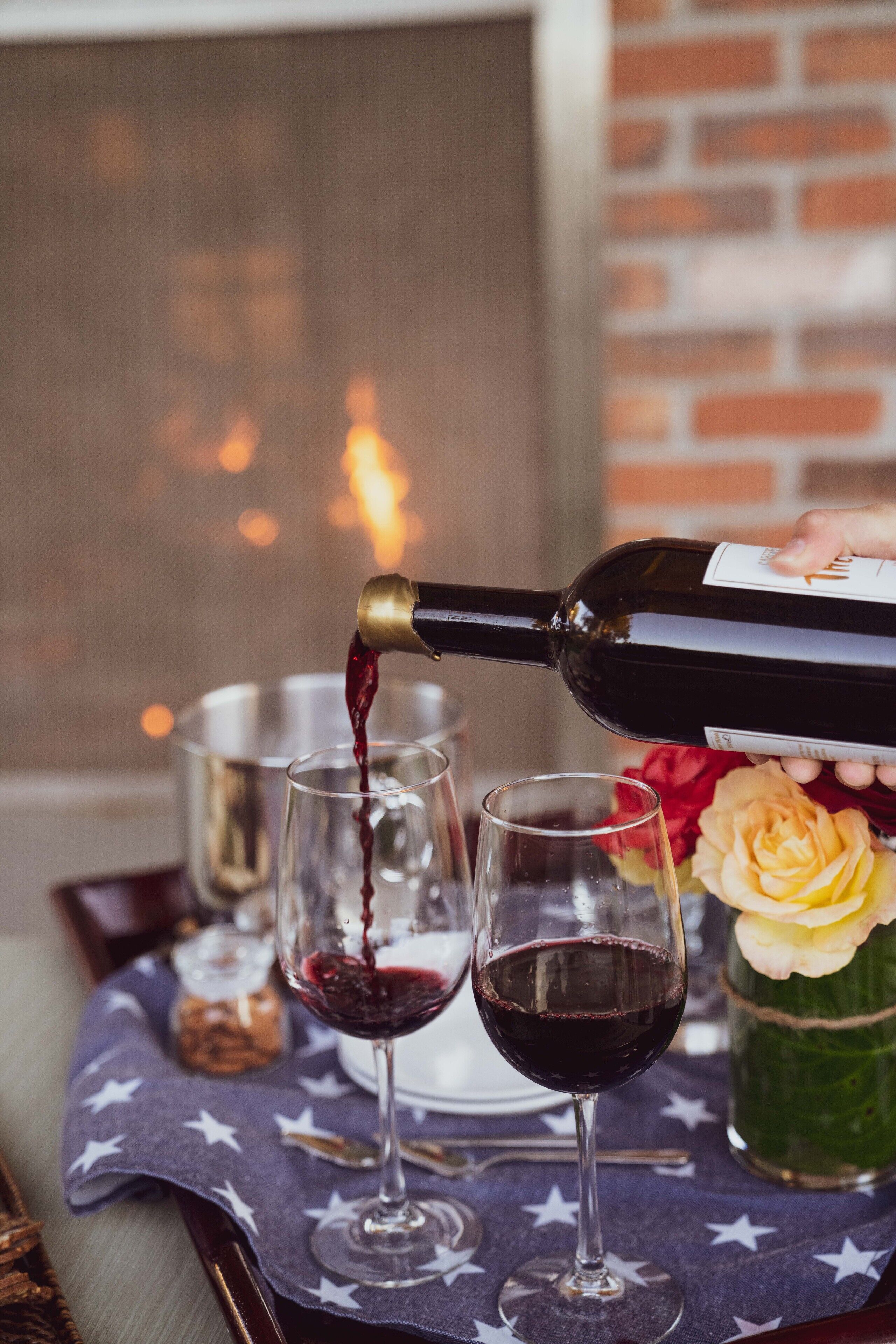 Una botella de vino tinto sirviéndose en dos copas sobre una mesa con mantel estampado de estrellas.